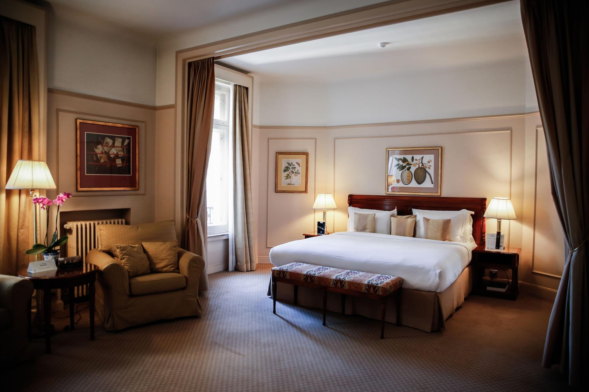 布鲁塞尔广场酒店  外观 照片 The photo shows a well-decorated bedroom. It features a large bed with white linens and several pillows, positioned against a wall with framed artwork above it. On either side of the bed, there are lamps providing soft lighting. There’s a cozy seatin
