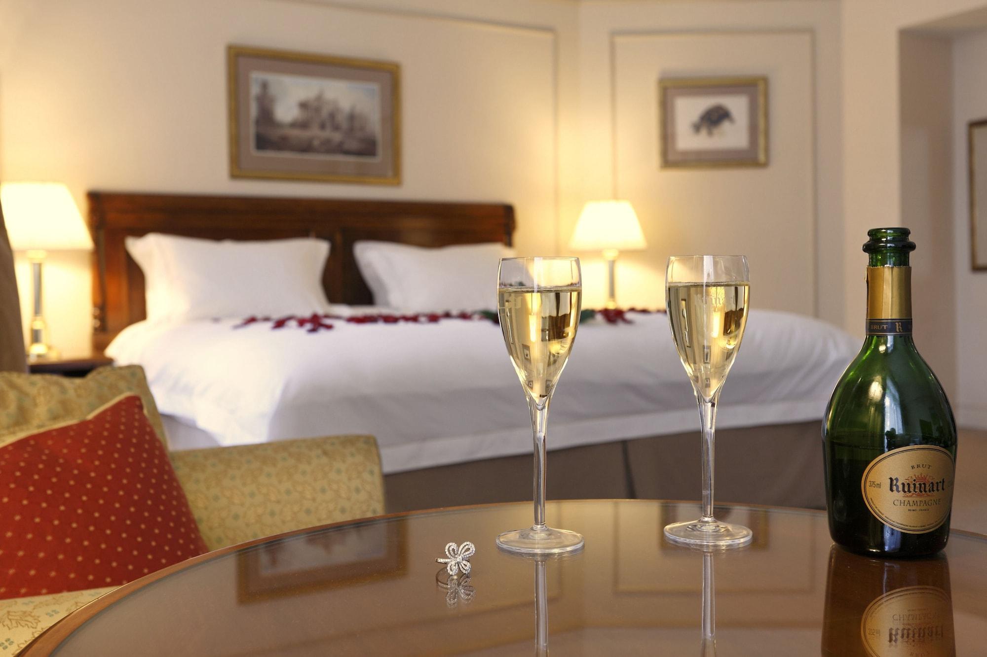 布鲁塞尔广场酒店  外观 照片 The image shows a cozy hotel room with a large bed adorned with decorative pillows and a romantic touch of rose petals. In the foreground, there are two champagne glasses filled with bubbly drinks, placed on a polished table. Next to the glasses, the