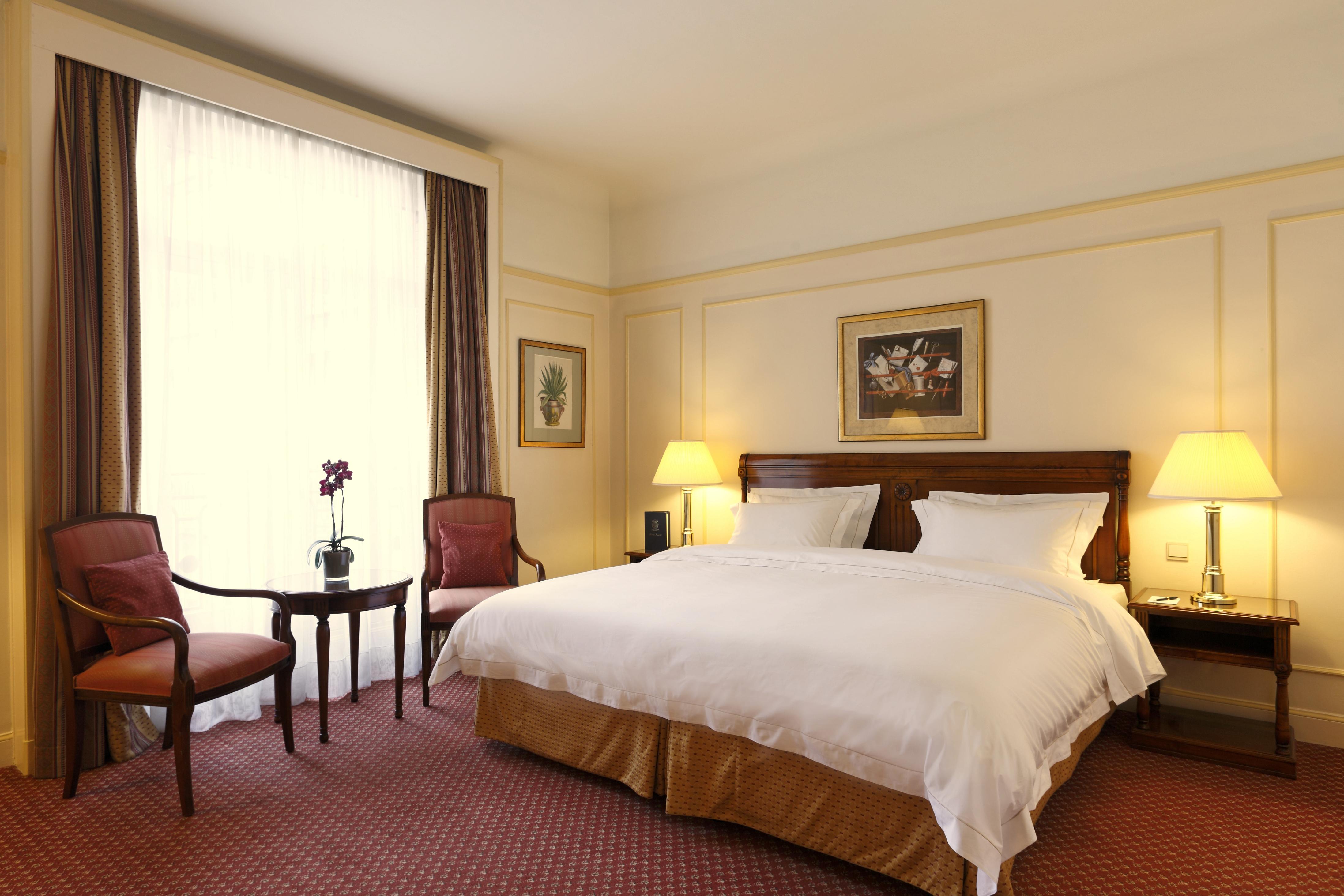 布鲁塞尔广场酒店  外观 照片 The photo shows a cozy hotel room featuring a double bed with white bedding and a gold accent at the base. To the sides of the bed, there are two bedside lamps providing soft lighting. There are two upholstered chairs and a small round table position