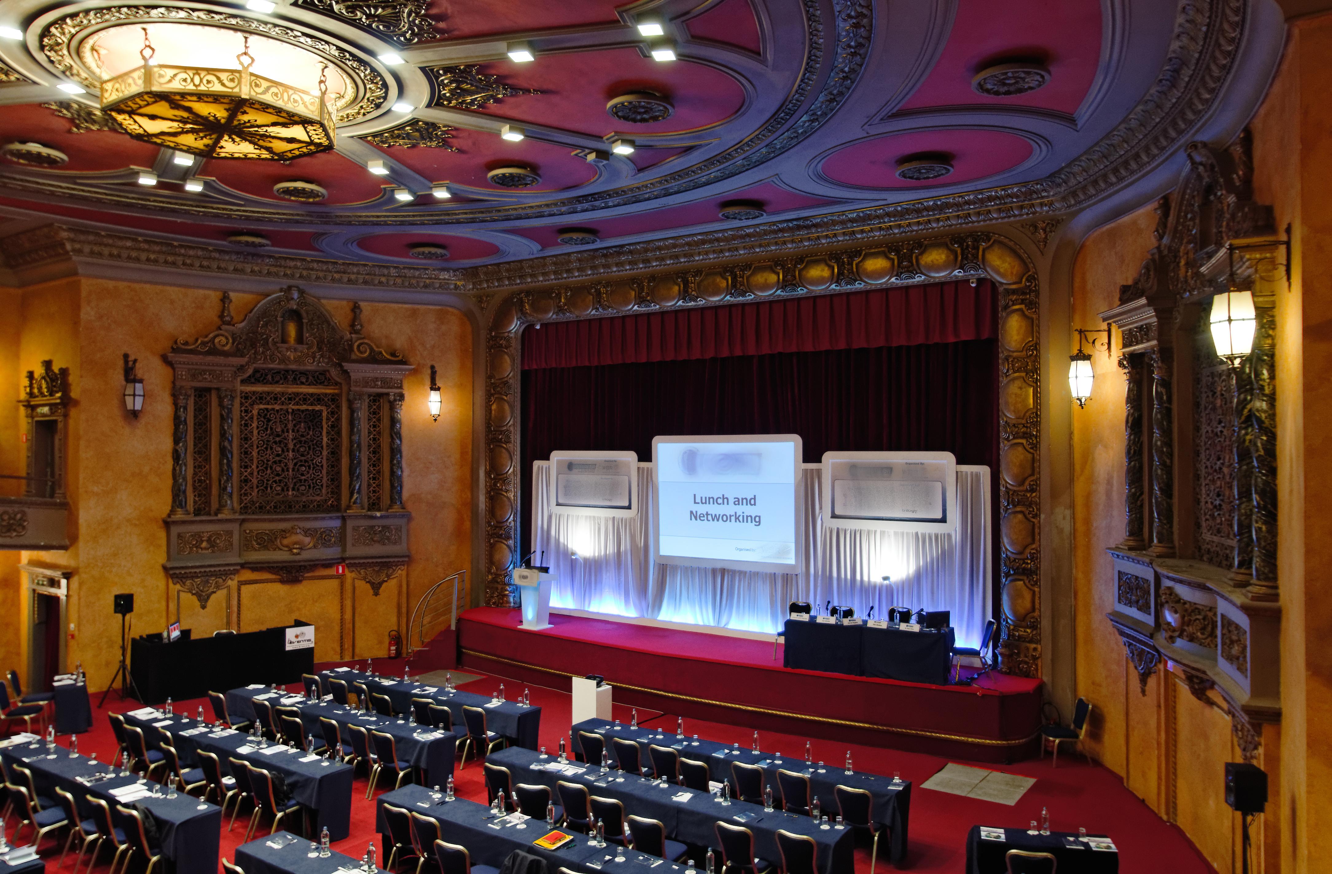 布鲁塞尔广场酒店  外观 照片 The photo shows a spacious banquet or conference hall with a stage set up for an event. The stage features a large screen with the words "Lunch and Networking" displayed prominently. In front of the stage, there are several rows of neatly arranged ta