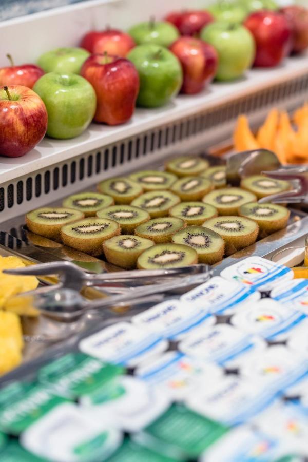 布鲁塞尔广场酒店  外观 照片 The photo shows a selection of sliced kiwifruit arranged neatly on a metal tray. The slices reveal the green flesh with tiny black seeds in the center. In the background, there are also whole apples, and nearby, there seems to be additional fruit, po