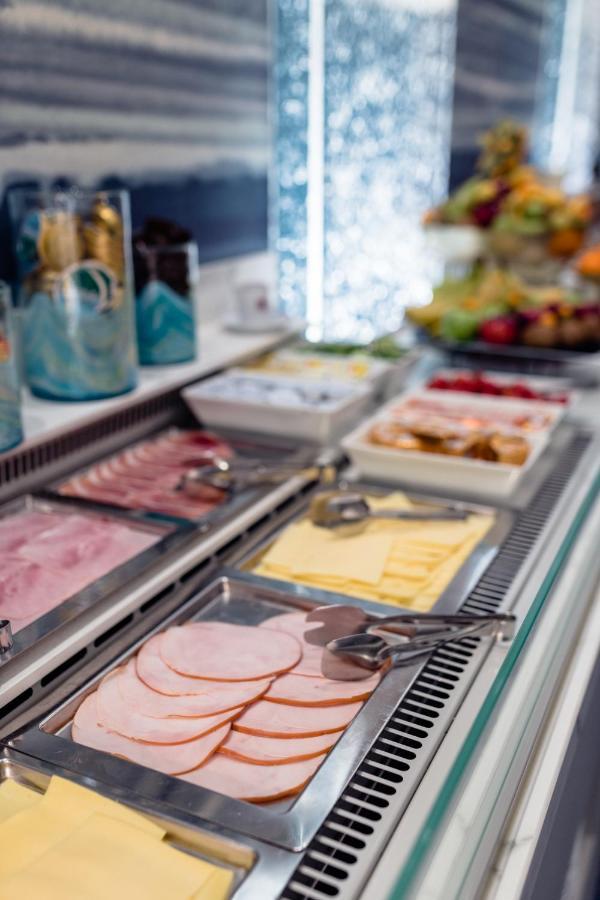 布鲁塞尔广场酒店  外观 照片 The photo shows a buffet spread featuring various types of cold cuts and cheeses. There are neatly arranged trays with different kinds of sliced meats, such as ham, along with slices of yellow cheese. Additionally, there are utensils, like tongs, ava