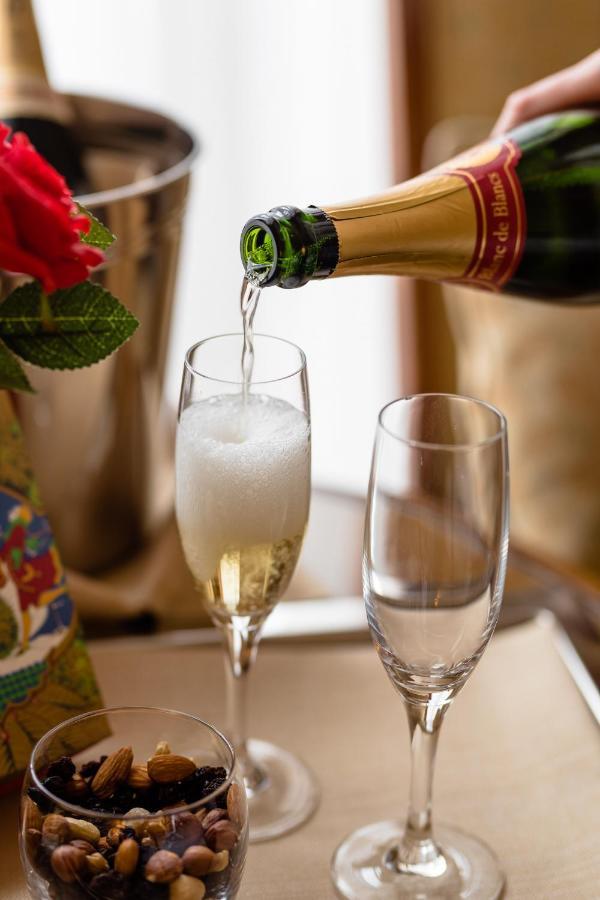 布鲁塞尔广场酒店  外观 照片 The photo shows a bottle of sparkling wine being poured into a champagne flute. The glass is slowly filling with bubbly liquid, creating a frothy head. Next to the flute, there is an empty glass, and there are some decorative elements in the backgrou