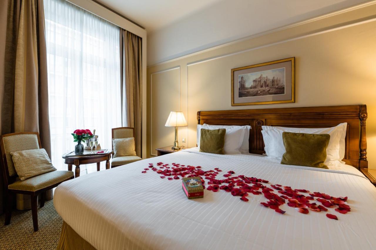 布鲁塞尔广场酒店  外观 照片 The photo shows a cozy and elegantly designed hotel room. There is a large bed with white linens, adorned with green pillows. Petals from red flowers are scattered across the bed, creating a romantic atmosphere. Beside the bed, there are two chairs a