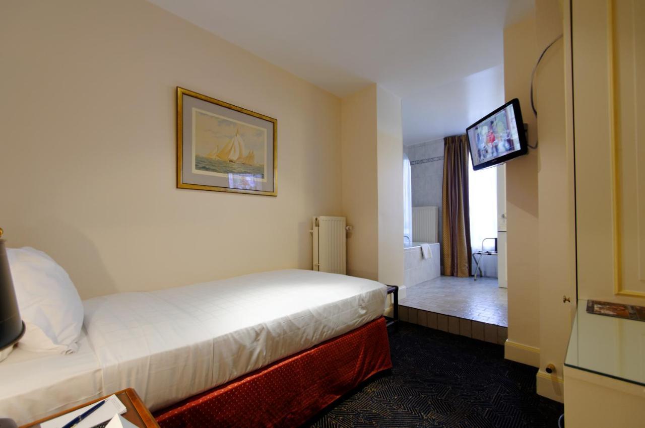 布鲁塞尔广场酒店  外观 照片 The photo shows a small hotel room featuring a single bed with white linens and a dark red bed skirt. There's a painting on the wall above the bed. A flat-screen television is mounted on the wall across from the bed. To the right, there's a doorway t