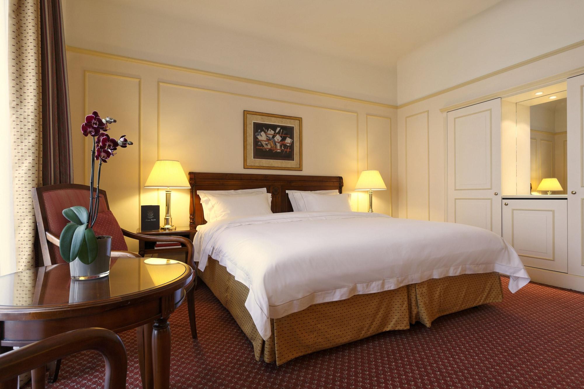 布鲁塞尔广场酒店  外观 照片 The photo shows a cozy hotel room featuring a large bed with white linens and a golden bed skirt. On either side of the bed, there are bedside lamps providing warm light. There's a small table with a vase containing purple orchids, adding a touch of 