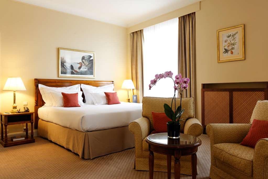 布鲁塞尔广场酒店  外观 照片 The photo shows a well-decorated hotel room. It features a large bed with white bedding and red accent pillows. There are two bedside lamps on either side of the bed. A seating area includes a comfortable armchair and a small round table with a potte