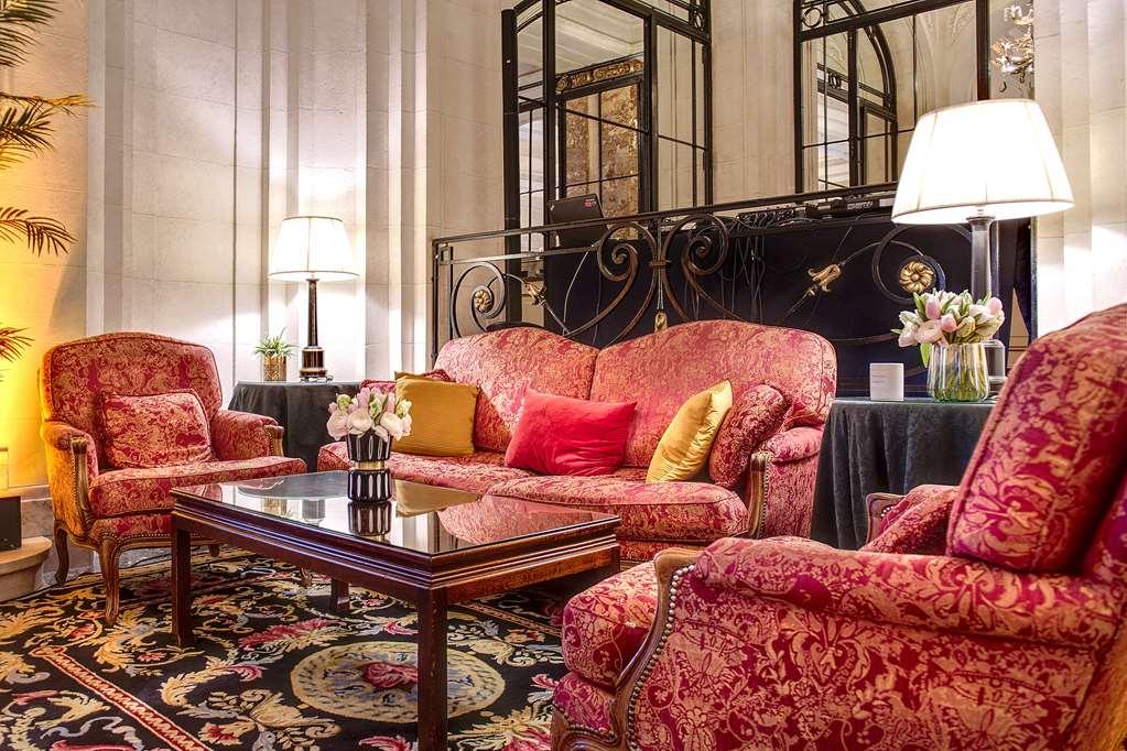 布鲁塞尔广场酒店  内观 照片 The photo shows an elegantly decorated seating area or lounge. There are several plush armchairs and a couch upholstered in rich, patterned fabric, primarily in shades of red and gold. They are arranged around a polished wooden coffee table. The tabl