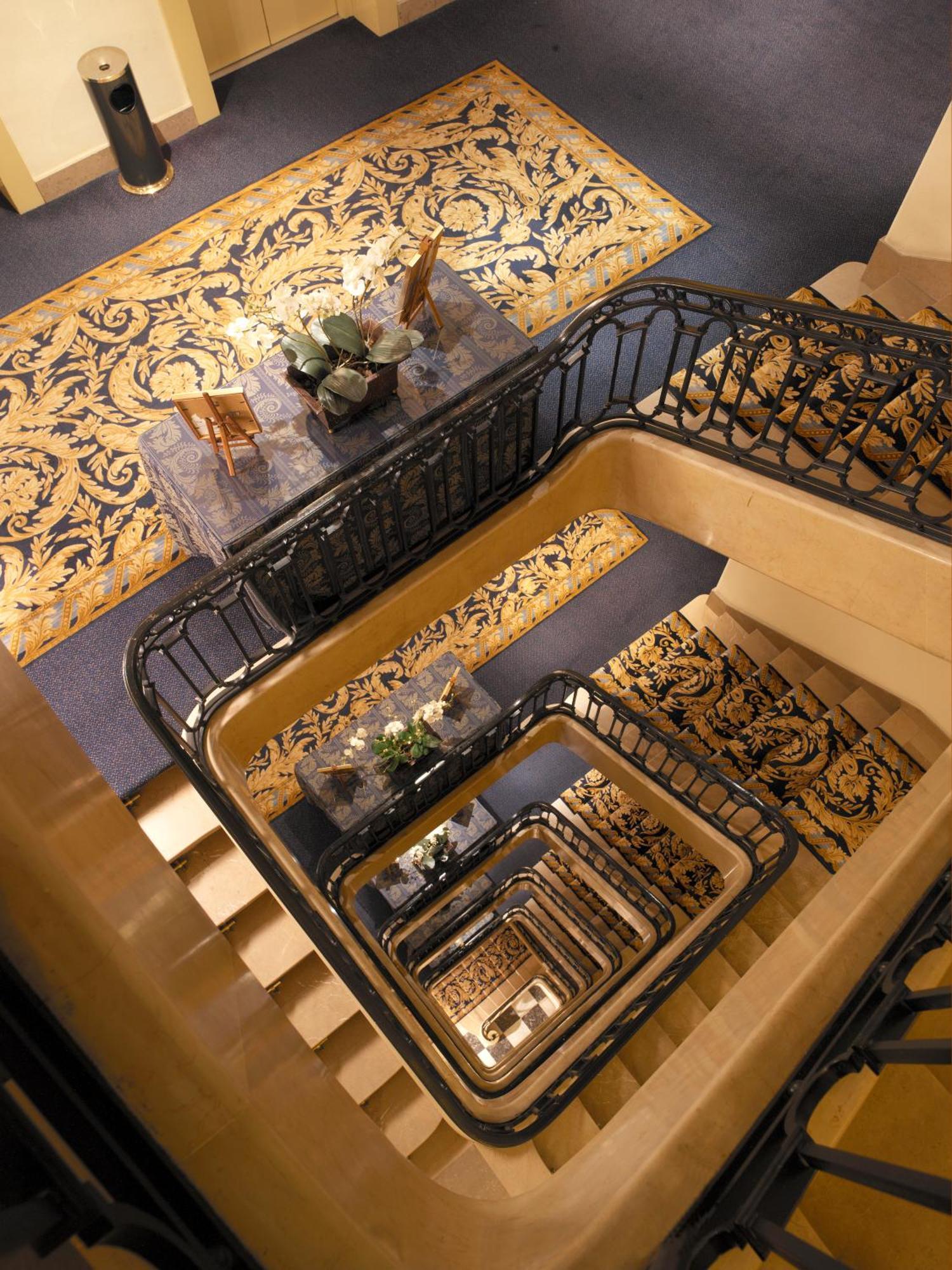 布鲁塞尔广场酒店  外观 照片 The photo shows a staircase viewed from above, featuring a series of descending steps that curve around a central area. The walls and railings are elegantly designed, with a decorative black metal railing. At the top of the stairs, there is a small t