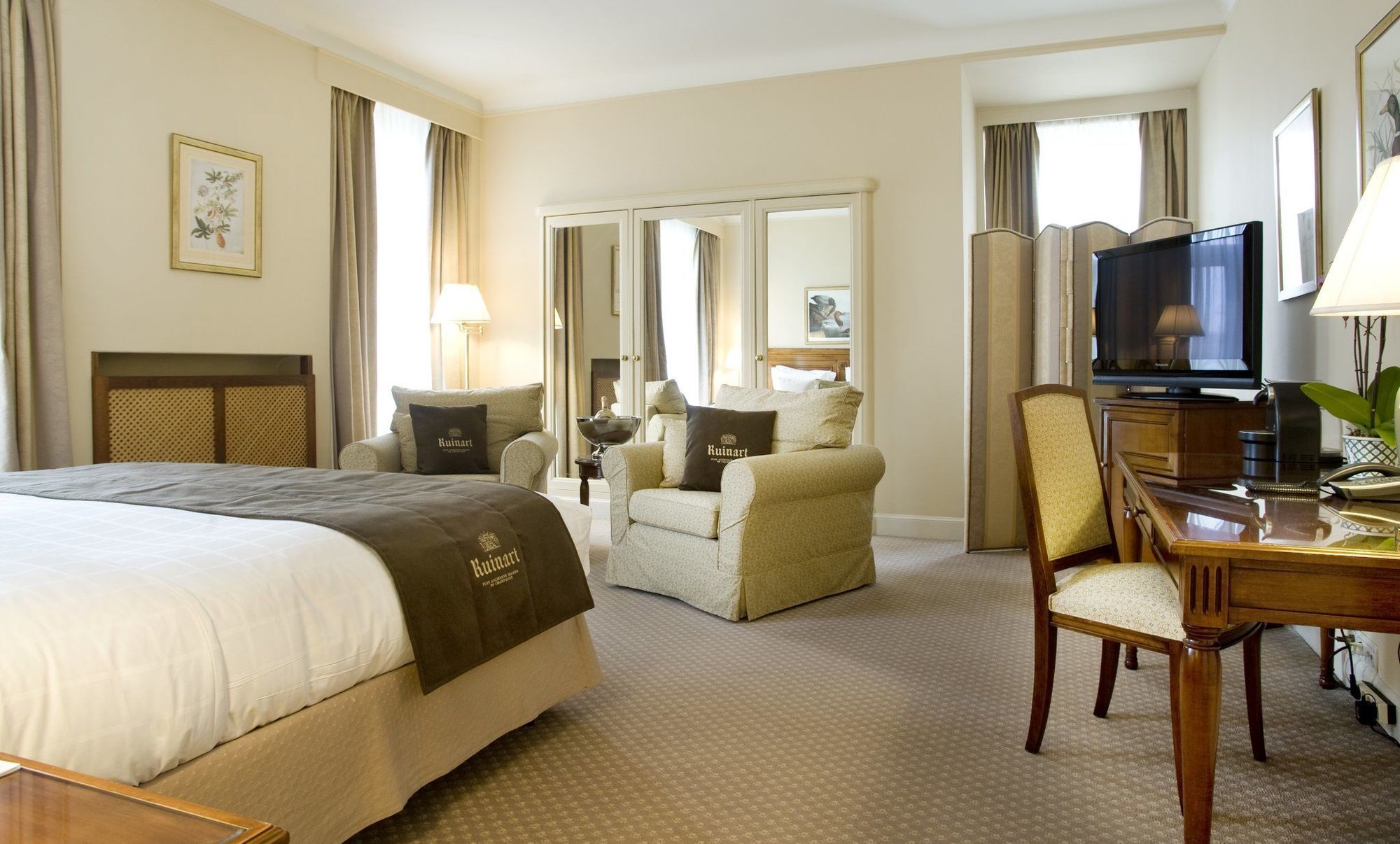 布鲁塞尔广场酒店  客房 照片 The photo shows a well-appointed hotel room. It features a large bed with a white duvet and a dark brown throw blanket at the foot. Beside the bed, there is a lamp providing soft lighting. A pair of curtains frame the windows, allowing natural light 