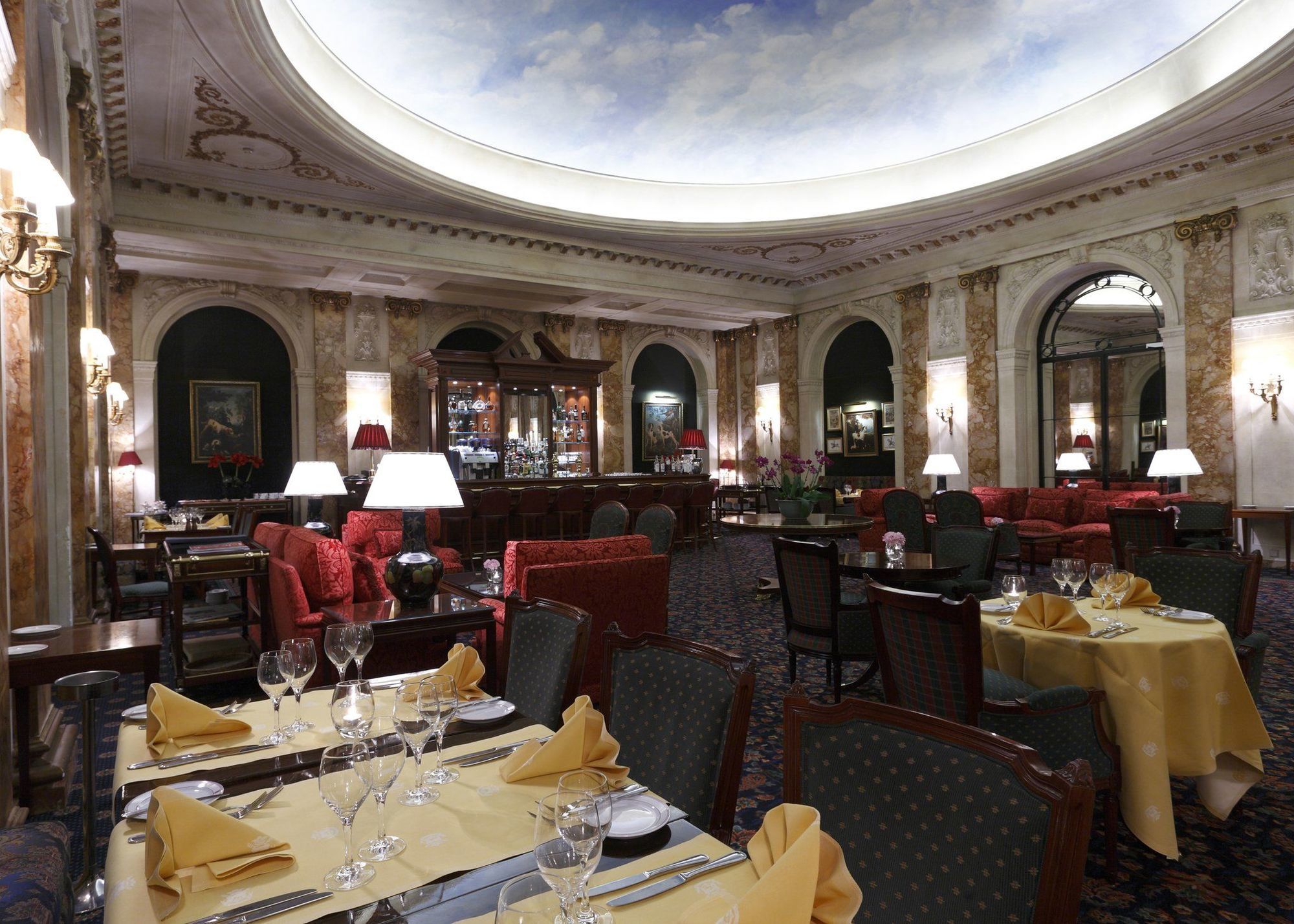 布鲁塞尔广场酒店  餐厅 照片 The image depicts a luxurious restaurant interior. It features elegantly arranged tables with yellow tablecloths and napkins. The seating area includes plush red couches and dark wooden chairs. The walls are adorned with ornate decorations, and there