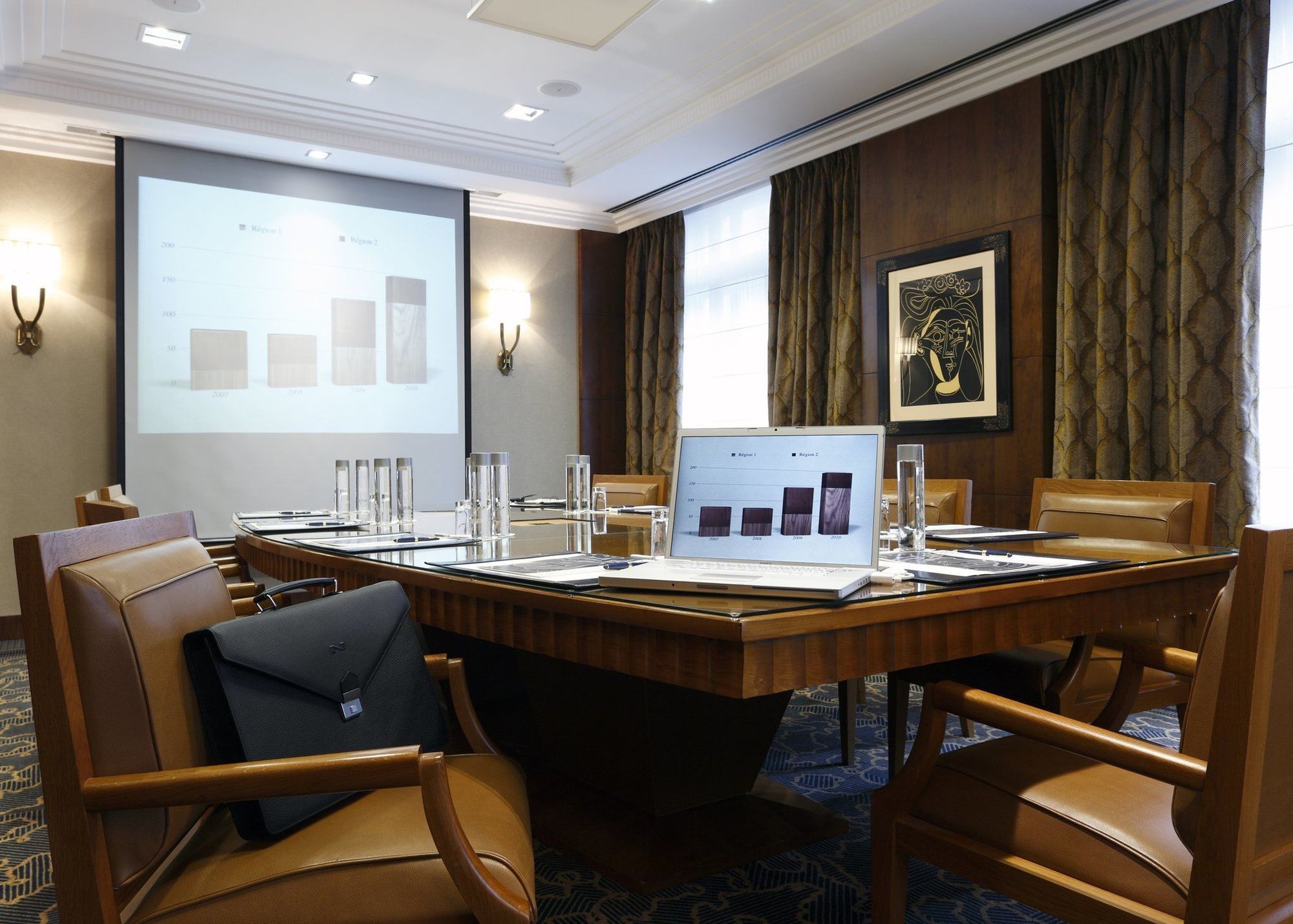 布鲁塞尔广场酒店  设施 照片 The image depicts a modern conference room. In the center, there is a large wooden table surrounded by several brown leather chairs. A laptop is positioned on the table, displaying a presentation or report. Behind the table, a screen shows a series o