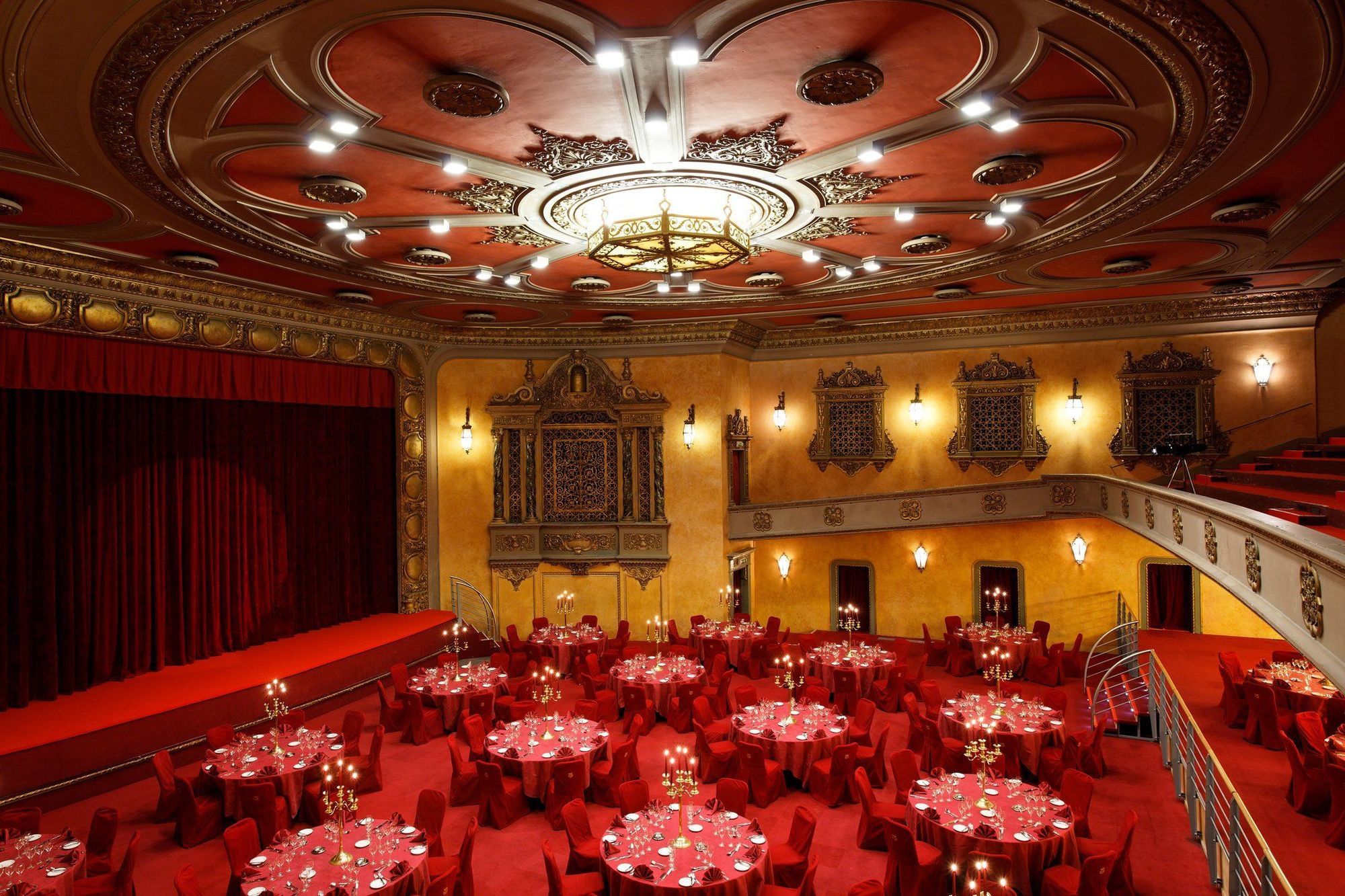 布鲁塞尔广场酒店  餐厅 照片 The photo shows an elegant theater interior, featuring a stage with red curtains and a beautifully designed ceiling with intricate details and lighting fixtures. Below the stage, there are round tables set with red tablecloths and candles, arranged i