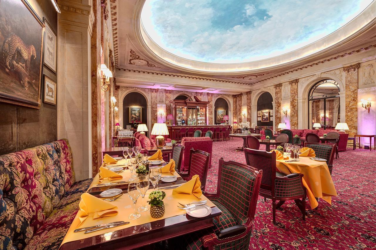 布鲁塞尔广场酒店  外观 照片 The photo shows an elegant restaurant interior with a luxurious ambiance. The space features a high ceiling with a painted or decorated skylight reminiscent of a clear blue sky. The tables are set neatly with yellow tablecloths, plates, and cutlery, 