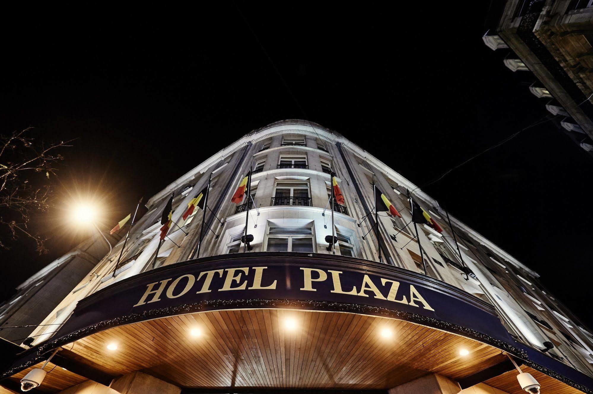 布鲁塞尔广场酒店  外观 照片 The photo shows the exterior of a hotel called "Hotel Plaza." It is taken at night, and the hotel has a prominent entrance that features a curved facade. The building is illuminated by exterior lights, highlighting its architecture. There are flags d