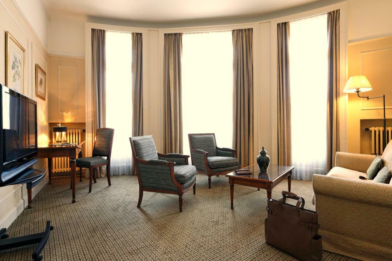 布鲁塞尔广场酒店  外观 照片 The photo shows a cozy sitting area in a room with large windows that allow natural light to fill the space. There are four comfortable chairs arranged around a wooden coffee table, and a small decorative object is placed on the table. A sofa is also
